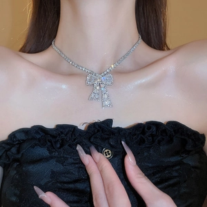 Close-up of sparkling silver bow necklace with zircons worn by a model in warm light