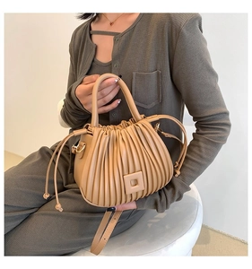 Close-up of pleated beige bucket bag showing the texture, handle, and adjustable strap