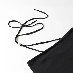 Detail of black halter top featuring white pearl accent and delicate strap stitching