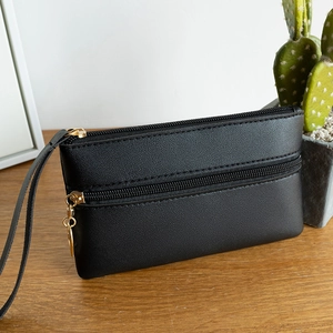 Minimalist black faux leather clutch bag with double gold zippers on wooden table