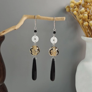 Detailed view of long tassel earrings with black teardrop pendants on wooden branch
