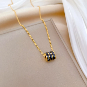 Close-up of a gold cylinder pendant with black baguette stones on beige silk