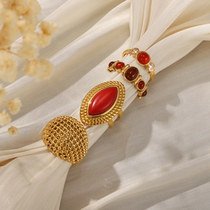 Set of four gold-plated stainless steel rings with red gemstones on silk background