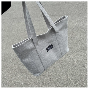 Close-up of gray woven tote bag featuring a black fashion label and textured fabric