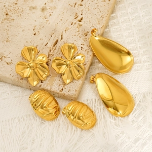 Set aus goldenen Edelstahl-Ohrringen in Blumen- und Tropfenform auf Steintablett