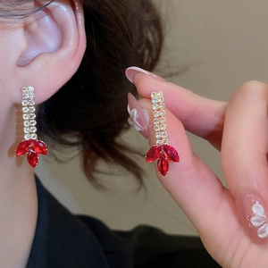 Close-up of golden tassel earrings with red teardrop zircon stones on elegant model