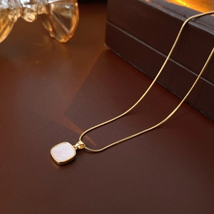 Gros plan sur le collier à chaîne serpent dorée avec pendentif carré en nacre blanche
