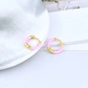 Macro shot of pink enamel and gold hoop earrings on a white marble display