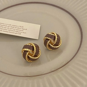 Macro detail of vintage gold twist earrings with brown enamel on a ceramic plate