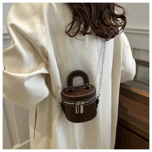 Détail du sac cylindre en cuir marron foncé avec fermeture éclair argentée et coutures blanches