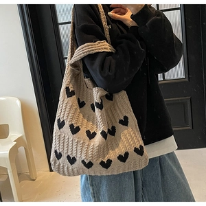 Bolso de hombro de punto con motivo de corazón negro mostrado colgado del hombro