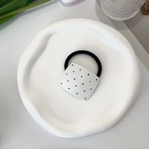Detail of square white hair tie with colorful polka dots on a minimalist tray