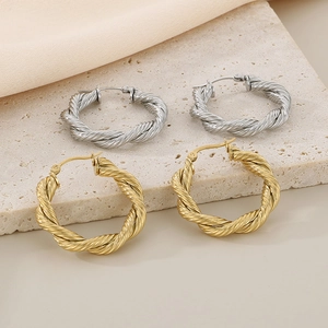 Macro view of gold and silver twisted hoop earrings on textured stone and satin fabric