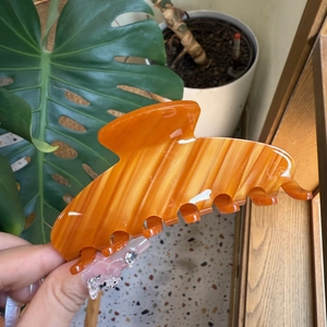 Detail of amber acetate claw clip with marble texture held in hand against home background