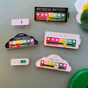 Detailed view of colorful social battery and mood tracker enamel pins on a soft green background