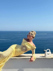 Detail of yellow off-shoulder dress with lace sleeves against a scenic ocean background