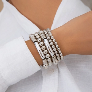 Detail of layered silver metal bracelets with beaded charms worn on a wrist