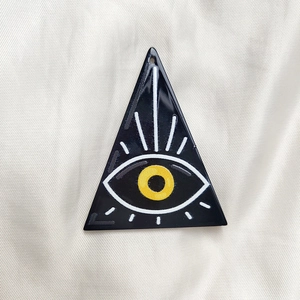 Detail of triangular acrylic evil eye pendant with black base and yellow iris detail