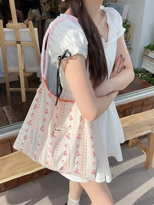 Floral canvas tote bag with pink flower print and checkered straps in a garden setting