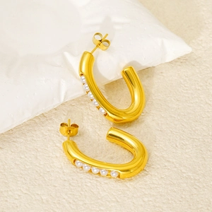 Detailed close-up of U-shaped gold earrings with embedded white pearls on textured background
