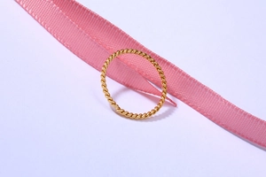 Detail eines gedrehten 18K Goldrings mit Spiralstruktur auf elegantem rosa Seidenband
