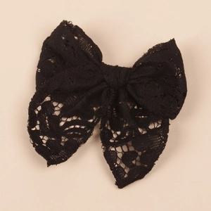 Detailed view of a black hollow lace bow hair clip for children on beige background
