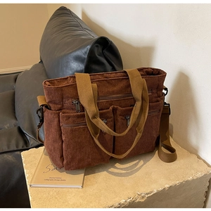 Detail of a brown corduroy multi-pocket tote bag with canvas straps on a stone stand