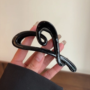 Close-up of a glossy black heart-shaped acetate hair claw clip held by a hand