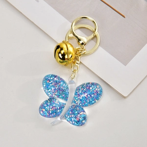 Detail view of blue glitter butterfly keychain with gold bell and metal clasp on white surface