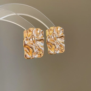 Macro shot of gold square earrings with irregular crinkled texture and metallic luster