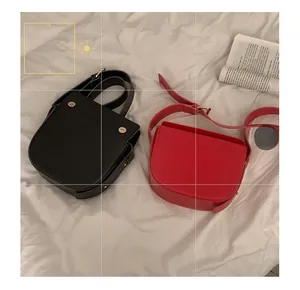 Flat lay of red and black PU leather saddle bags with wide straps on white fabric