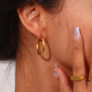 Close-up of twisted gold C-shaped hoop earrings and textured rings on a female model