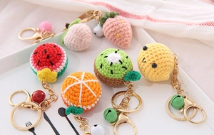 Close-up of handmade knitted fruit keychains with metal rings and bells on a tray