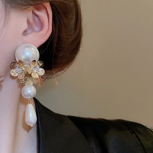 Close-up of pearl drop earrings with golden flower petals and shimmering crystals