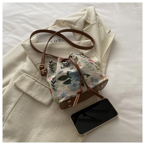 Detail of floral bucket bag with leather strap next to phone for size reference