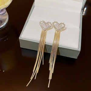 Elegant gold tassel earrings with rhinestone heart pendant hanging on a jewelry box edge