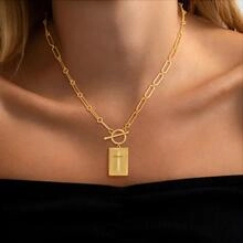 Close-up of gold paperclip chain necklace with a rectangle cross pendant and toggle clasp
