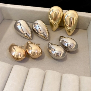Polished gold and silver teardrop stud earrings displayed in a grey velvet jewelry box