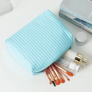 Light blue quilted cosmetic bag for travel showing organized skincare bottles and brushes