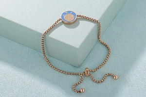 Dettaglio di un bracciale in oro rosa con chiusura a scorrimento e ciondolo zodiacale azzurro