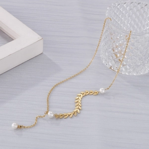Minimalist gold wheat leaf and pearl necklace on a textured gray background