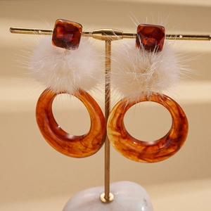 Detail of resin hoop earring with amber square piece and white fluffy pompom ball