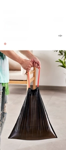 Close-up of thick black drawstring garbage bag showing material texture and red handles