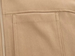 Détail de la texture en sergé kaki, fermeture éclair métallique et coutures des poches