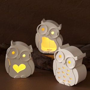 Three owl resin lamp covers with unique cut-outs emitting warm yellow light in dark setting