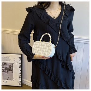 Detail of white quilted box bag with woven handle and gold chain on a black dress