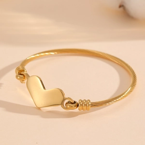 Détail d'un bracelet à breloque cœur doré avec un design de bracelet en câble torsadé