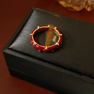 Detail of red enamel wavy ring with gold-plated beads on a textured jewelry box