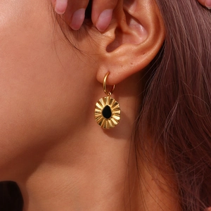 Close-up of gold hoop earrings with black droplet pendant worn by a model