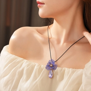 Close-up of a necklace with a blue flower pendant and purple teardrop gem on a black cord